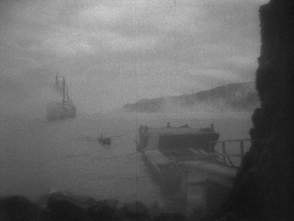 Island of Lost Souls (1932) movie still: A haunting monochrome wide shot captures a desolate coastal bay shrouded in dense fog, with a large,…