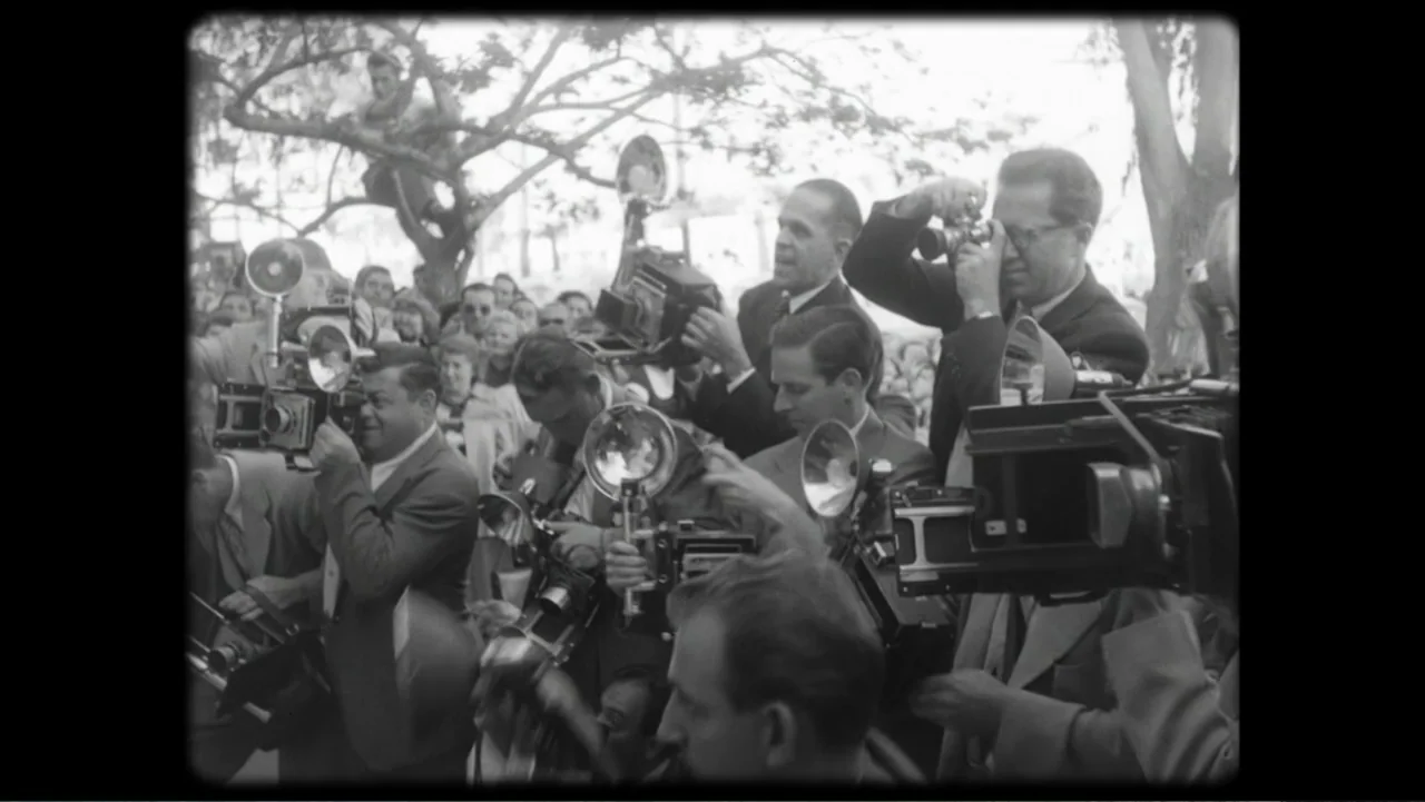 Elizabeth Taylor: The Lost Tapes (2024) movie still: medium — A crowd of people stand in an outdoor area filled with trees and foliage. Multiple…