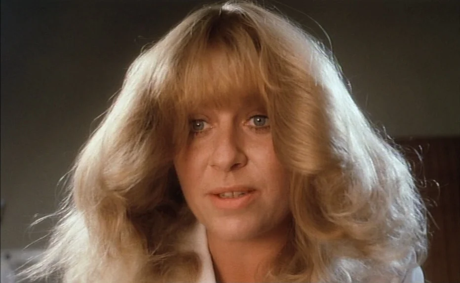 The Fourth Man (1983) movie still: closeup — An interior space with a plain, nondescript wall background. A woman with voluminous blonde hair faces…