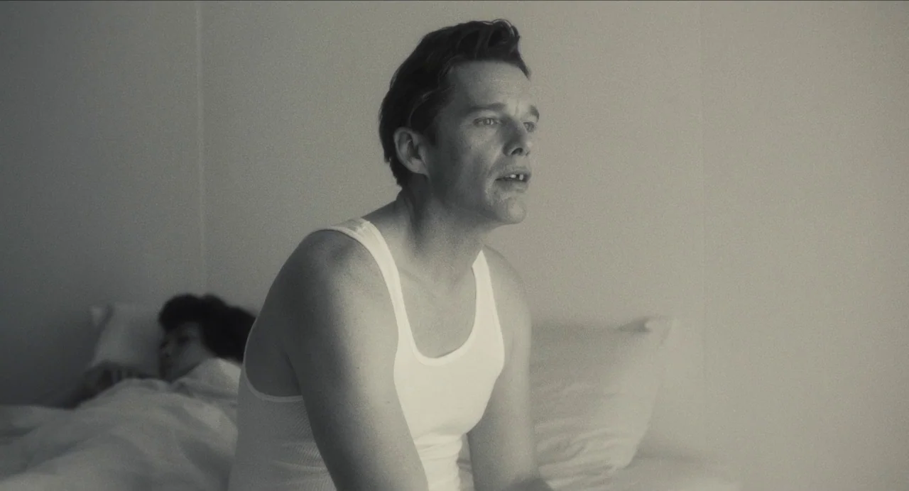 Born To Be Blue (2015) movie still: medium — A minimalist, brightly lit room with a stark white wall. A man sits on the edge of a bed while a woman…