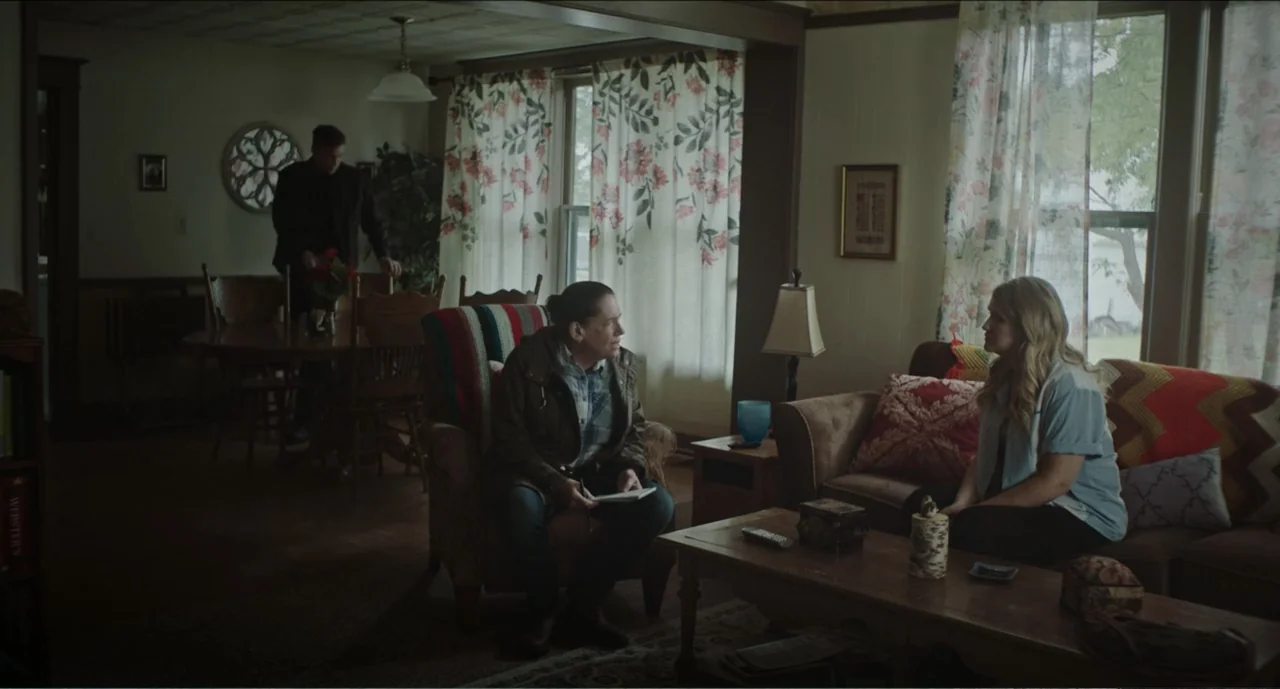 Cowboys (2014) movie still: medium — A dated home interior with floral curtains, wood paneling, and patterned upholstery. Two women converse in the…