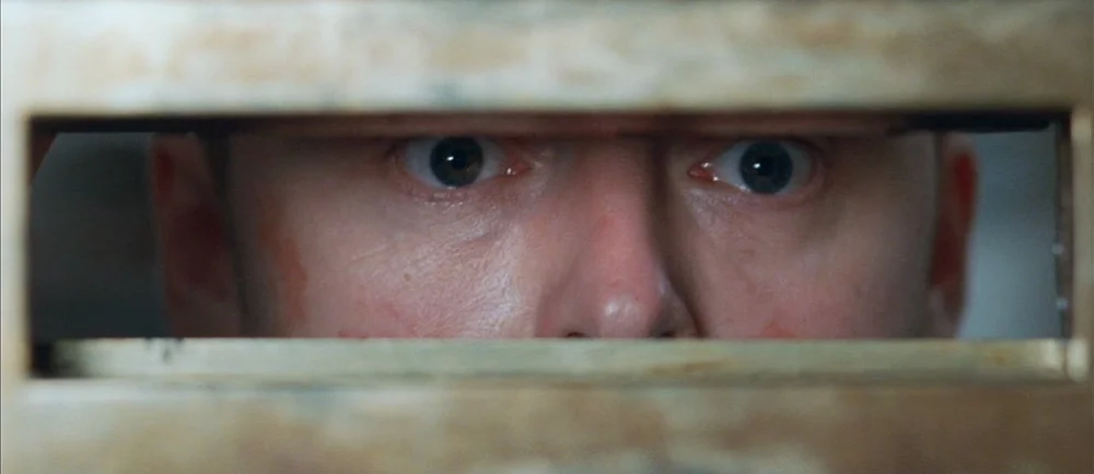 Shaun Of The Dead (2004) movie still: closeup — A metal letterbox slot provides a restricted view of a human face. A man gazes directly through the…