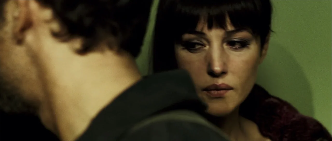 Shoot 'Em Up (2007) movie still: closeup — A close up over the shoulder shot of two people in a dark interior room. A woman with dark hair looks at…