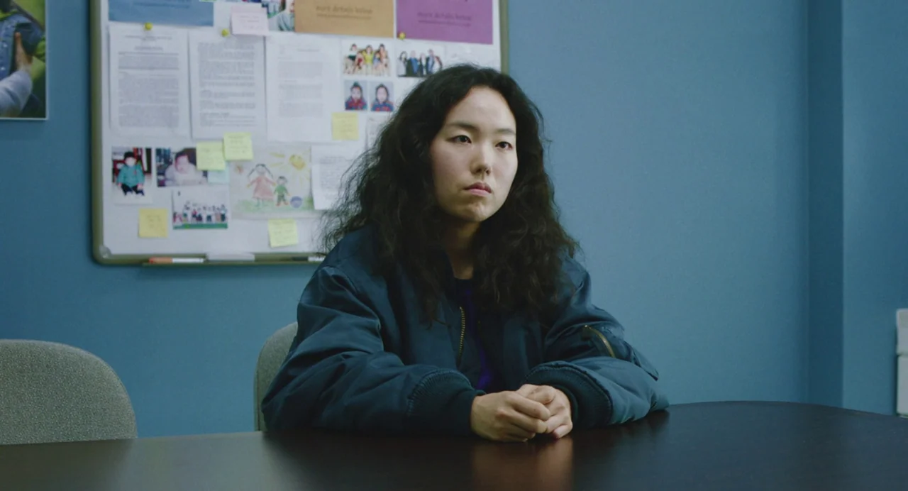 Return To Seoul (2022) movie still: medium — A blue-walled room features a large cork board covered in various notes and photos. A young woman with…