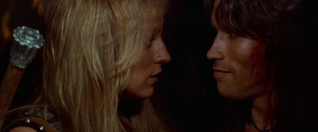Conan The Barbarian (1982) movie still: closeup — A dark environment provides little context other than two people standing face to face. The woman…
