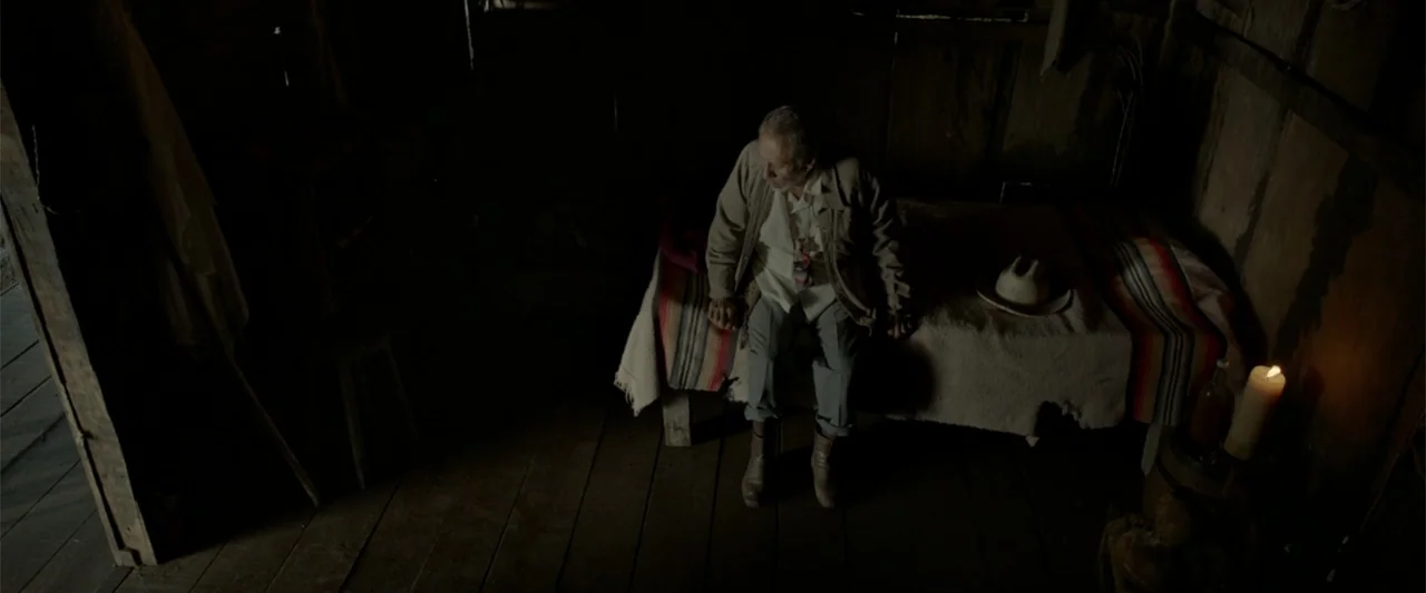 I Dream in Another Language (2017) movie still: medium — A dimly lit room with rough wooden walls and a plank floor. An elderly man sits on a narrow…