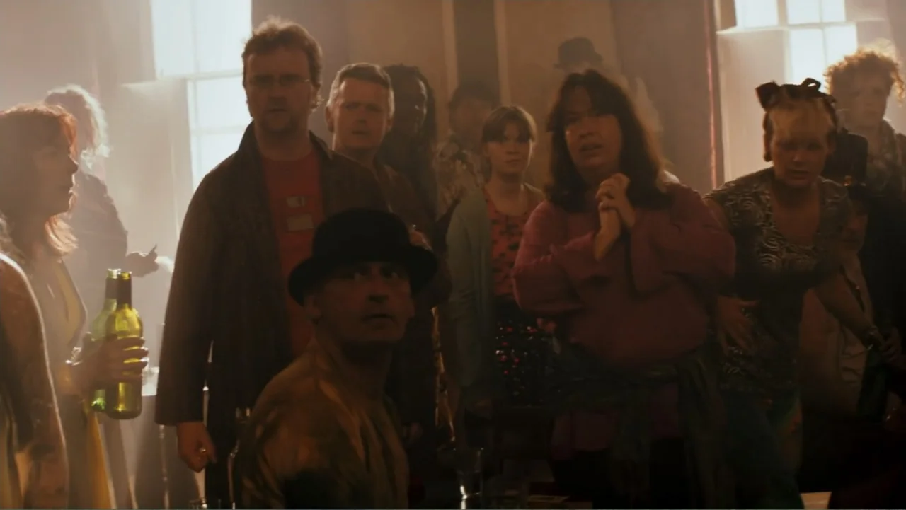 Robot Overlords (2015) movie still: medium — A crowded interior pub features people standing together amidst visible dust particles and haze. A…
