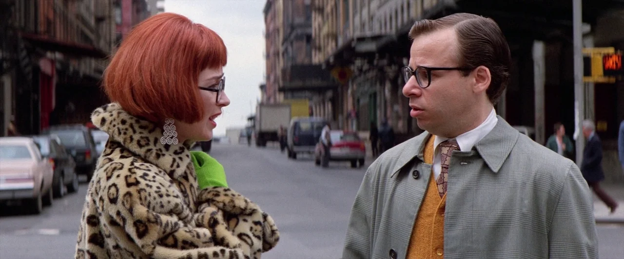 Ghostbusters 2 (1989) movie still: medium — A quiet city street is lined with parked cars and blurred urban storefronts. A woman in a leopard coat…