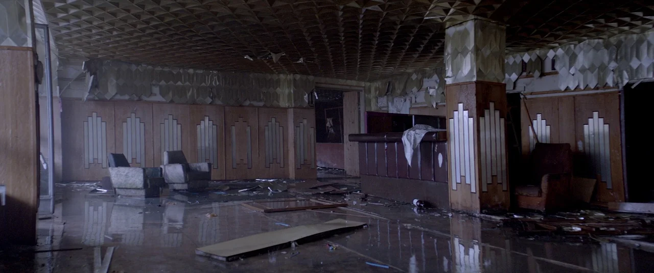 Loveless (2017) movie still: wide — A dilapidated, flooded hotel lobby features Art Deco wall panels and a textured ceiling. Debris litters the…