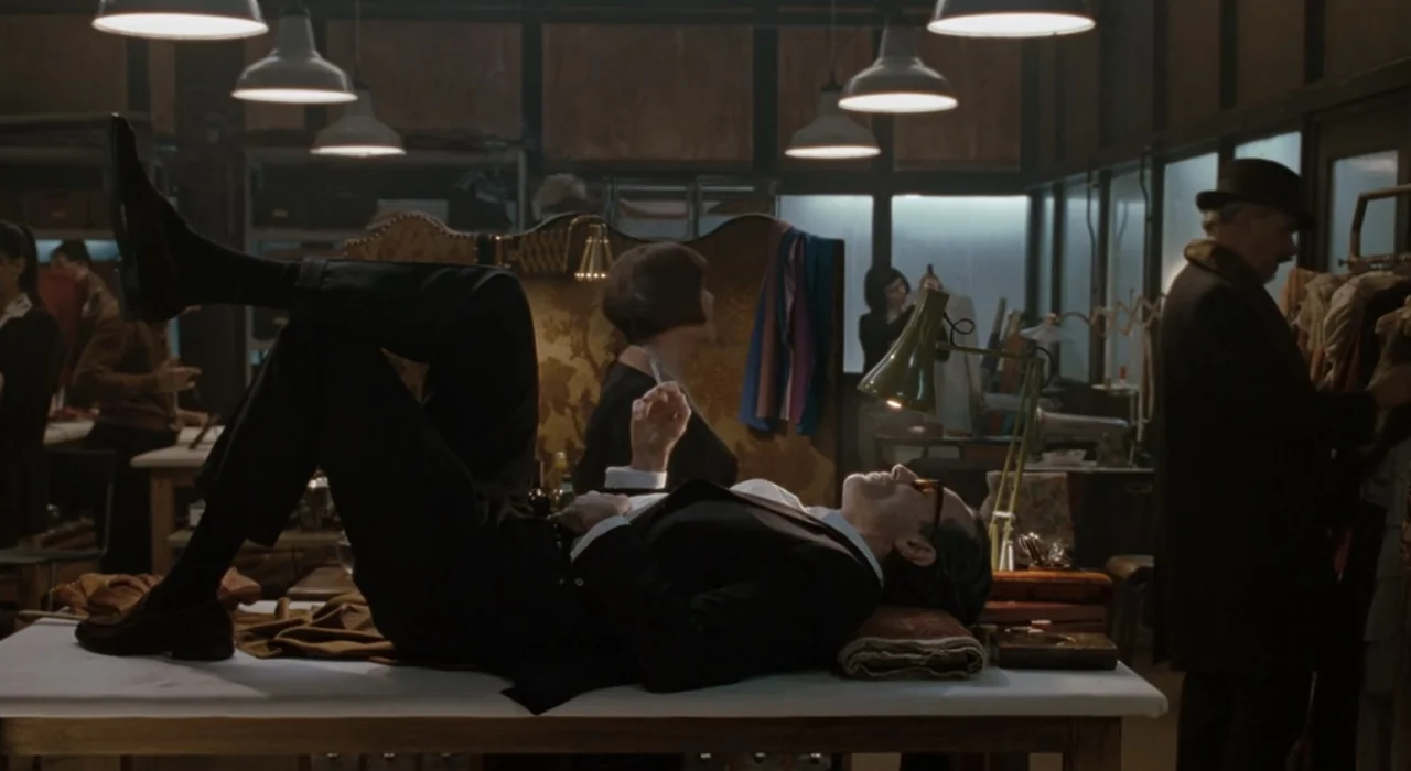 The Great Beauty (2013) movie still: medium — A cluttered workshop filled with garment racks and sewing tables under bright industrial lights. A man…