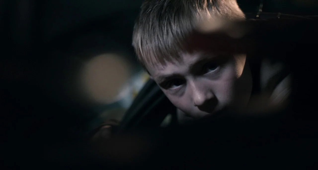 The Selfish Giant (2013) movie still: closeup — A dark, confined area provides limited visibility of the surroundings. A young boy looks directly…