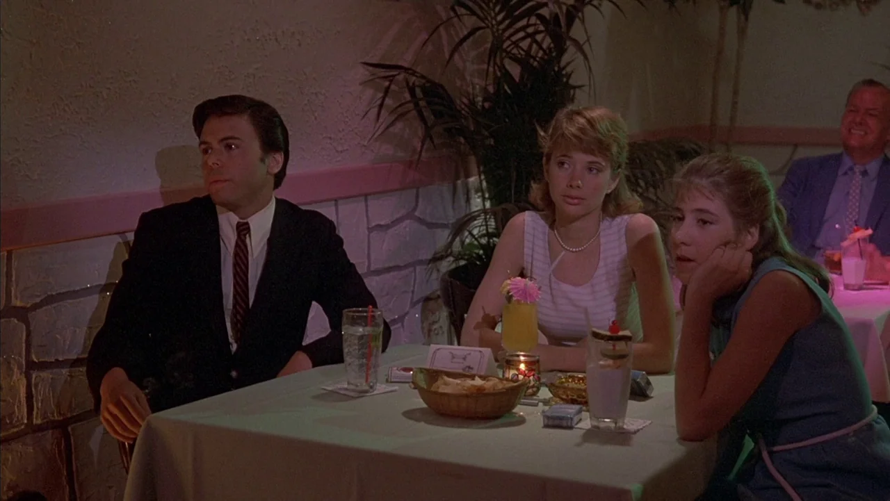 Baby It’s You (1983) movie still: medium — A restaurant interior features stone-textured walls and tropical foliage behind a dining table. Three…