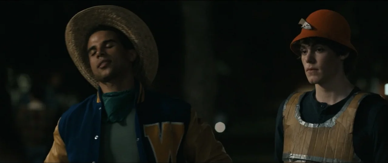 Scream VI (2023) movie still: medium — A dark outdoor space with indistinct background elements at night. Two young men stand side by side while one…