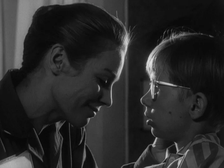 The Silence (1963) movie still: medium — An indoor space features low-key lighting focused on two figures in profile. A woman bends toward a young…