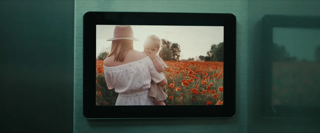 Double Blind (2023) movie still: closeup — A digital screen mounted on a textured, cool-toned wall displays a photograph. The photograph shows a…