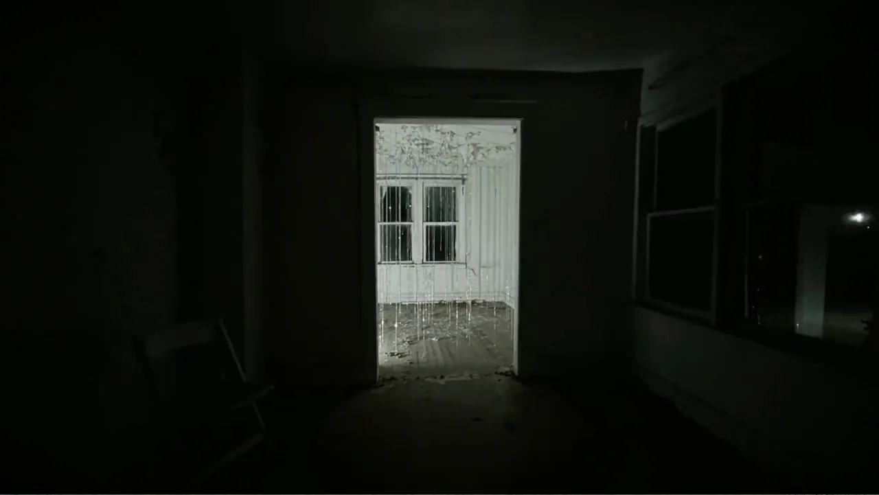 Inland Empire (2006) movie still: medium — An abandoned interior room with dark, empty walls and a solitary wooden chair. A bright light shines…