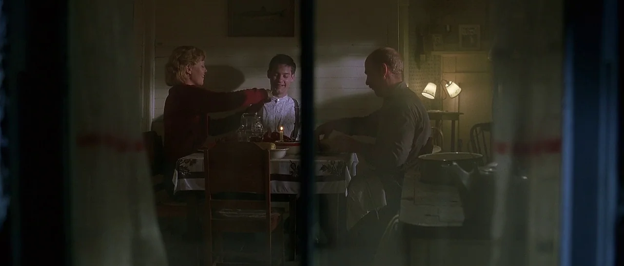 The Cider House Rules movie still: wide — A dimly lit room with wood-paneled walls and a simple table setting for dinner. Three family members sit…