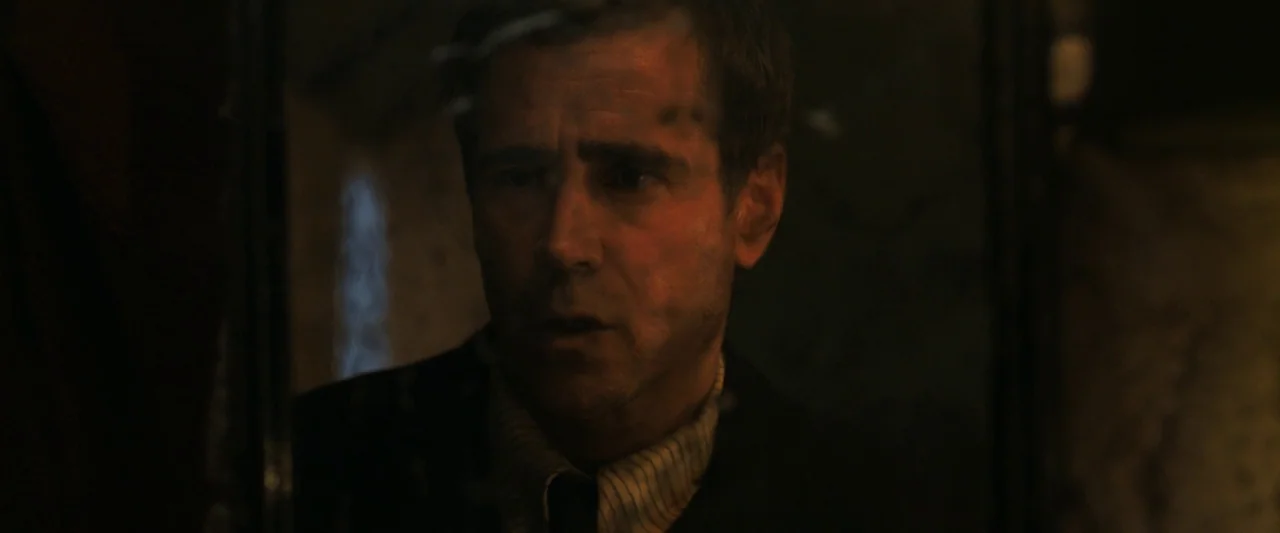 The Banshees of Inisherin (2022) movie still: closeup — A dark interior space with minimal light illuminating a man's face. He stares into the…