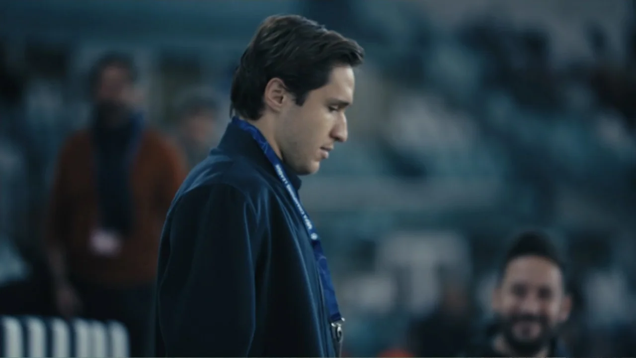 Federico Chiesa - Back on Track (2023) movie still: medium — A dark, blurred stadium interior with out-of-focus background figures in the stands. A…