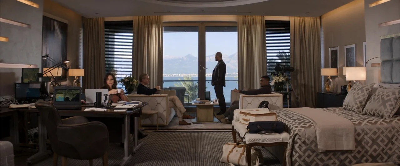 Operation Fortune: Ruse de Guerre (2023) movie still: wide — A spacious, modern hotel room overlooks the Mediterranean sea through floor to ceiling…