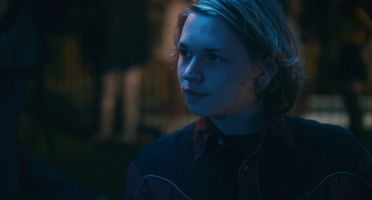 Palo Alto (2013) movie still: closeup — A person stands in a dimly lit environment filled with indistinct background movement and light. The subject…