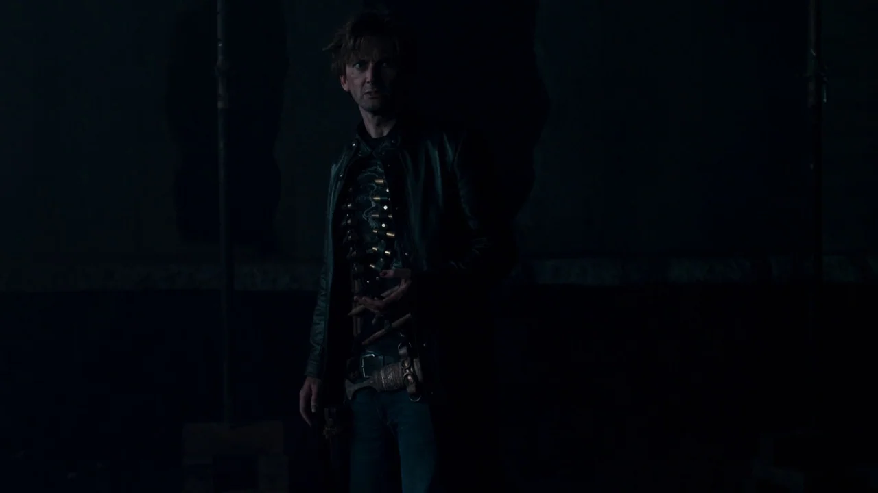 Fright Night (2011) movie still: medium — A dark, sparsely detailed interior space contains a man standing in shadow. He is positioned in the…