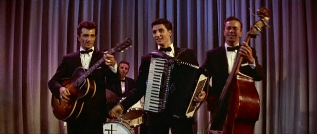 The Girl Can’t Help It (1956) movie still: medium — A group of musicians performs in front of a pleated fabric curtain backdrop. They wear matching…
