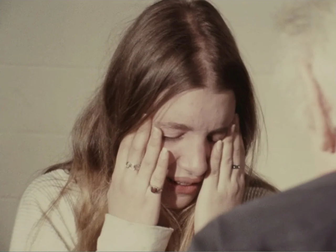 Don't Expect Too Much (2011) movie still: closeup — An interior space with a neutral-toned wall visible behind the subject. A young woman with long…