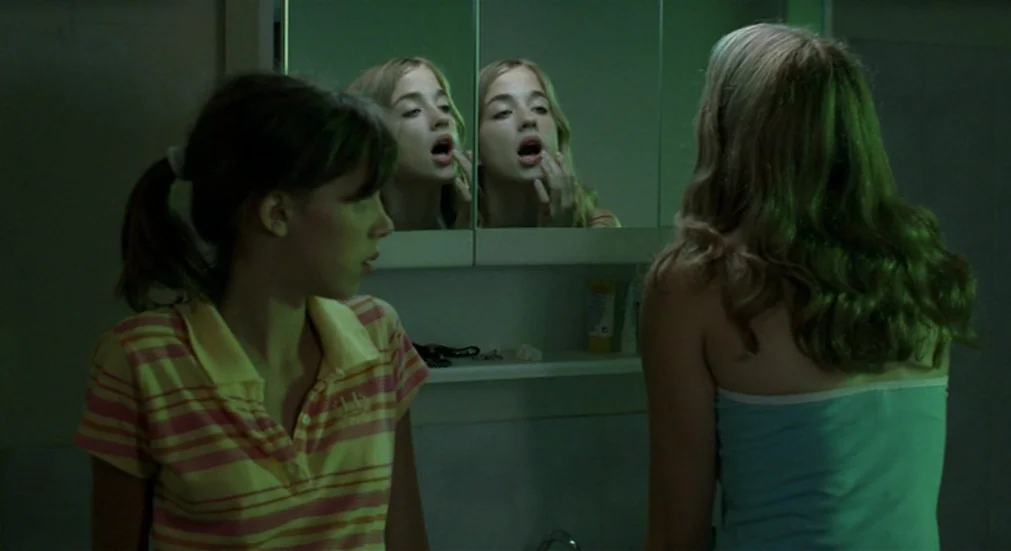 Water Lillies (2007) movie still: medium — A dimly lit bathroom features a mirrored medicine cabinet above the sink. Two teenage girls occupy the…