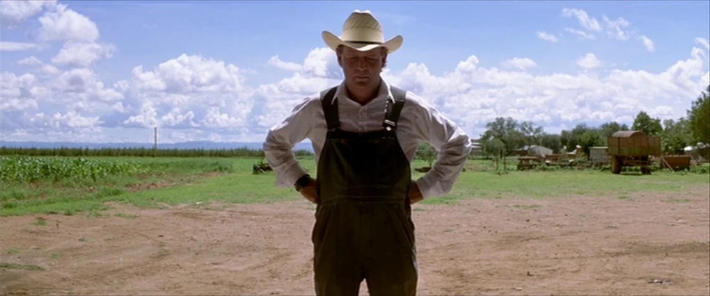 Silent Light (2007) movie still: fullbody — An open expanse of farmland features a single man standing in the foreground center. He stands on dirt…