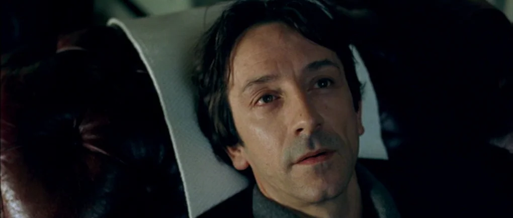 Mortal Transfer (2001) movie still: closeup — The interior of a vehicle features dark, tufted leather upholstery with a white headrest cover. A man…