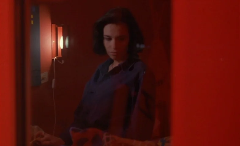 I Can’t Sleep (1994) movie still: medium — A woman in a blue shirt stands within a room with deep red walls. She looks downward while illuminated by…