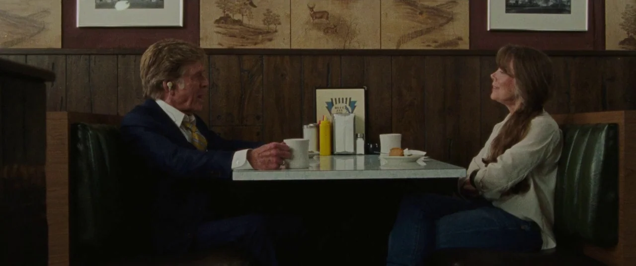 The Old Man & The Gun (2018) movie still: medium — A diner booth with dark wood paneled walls decorated with framed prints of wildlife. An elderly…
