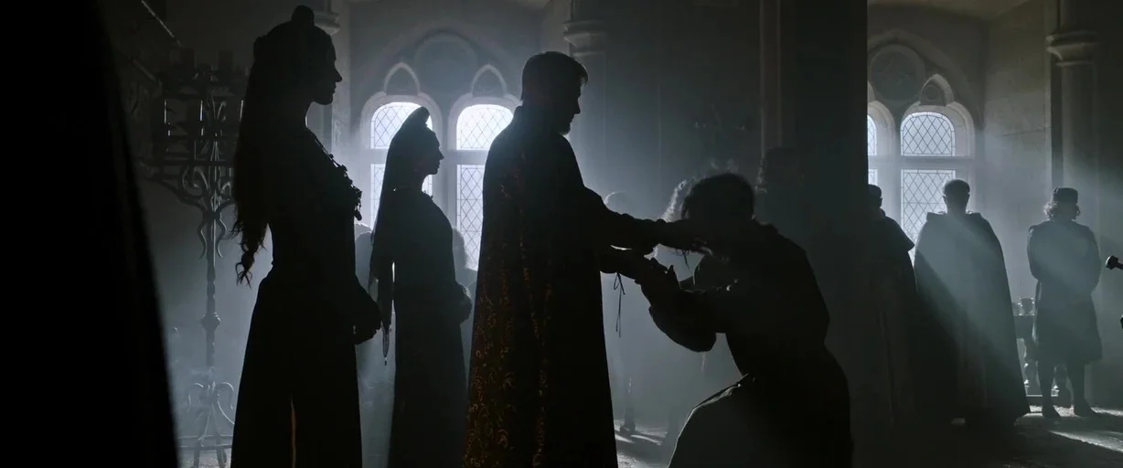 The Last Duel (2021) movie still: wide — A stone hall with arched windows and heavy mist filling the air. A man kneels before a noble figure as…