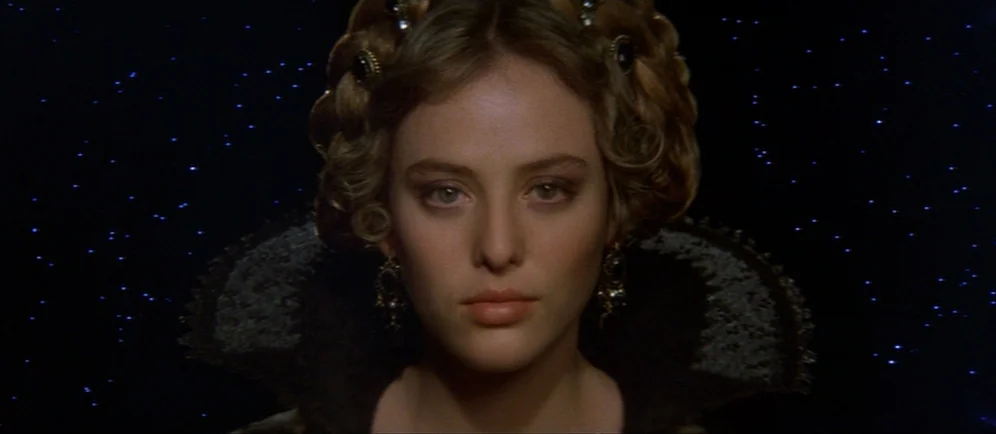 Dune (1984) movie still: closeup — A woman is centered against a dark void filled with tiny pinpricks of light. She stares directly forward in a…