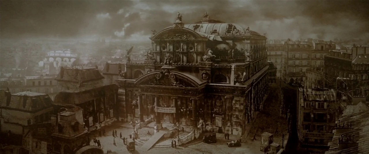 The Phantom of the Opera (2004) movie still: establishing — A large ornate opera house sits in the center of a dense urban square. Stormy clouds…