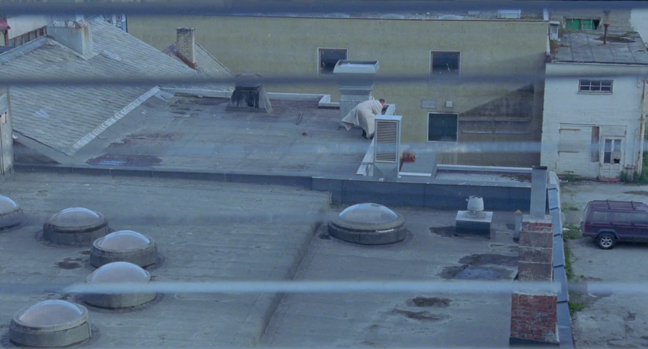 Insomnia (1997) movie still: wide — A flat concrete building roof features several circular skylight domes and ventilation equipment. A man wearing…