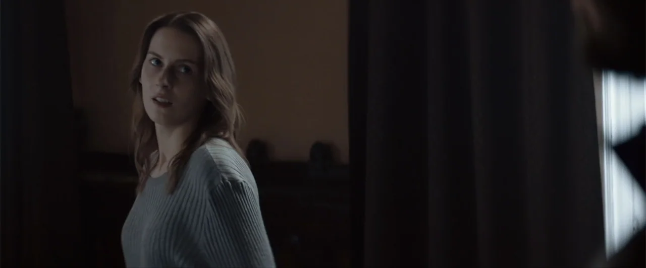 La herencia (2010) movie still: medium — A dimly lit room features heavy dark curtains and subtle architectural details in the background. A woman…