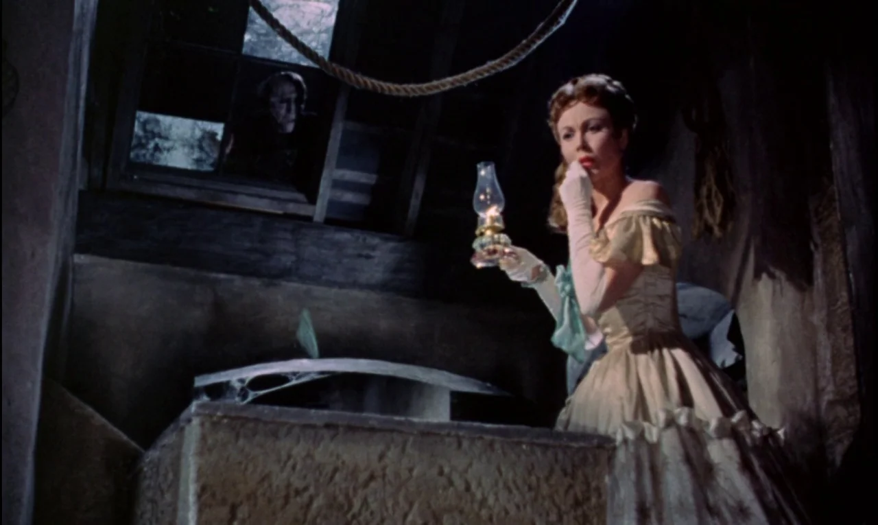 The Curse of Frankenstein (1957) movie still: medium — A dimly lit attic with wooden beams features a woman standing by a table. Through a window…