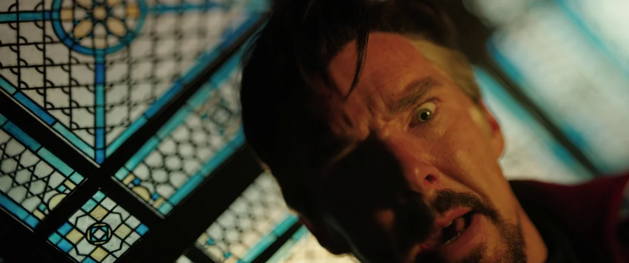 Doctor Strange in the Multiverse of Madness (2022) movie still: closeup — A high-angle perspective frames a man against a large blue-toned stained…