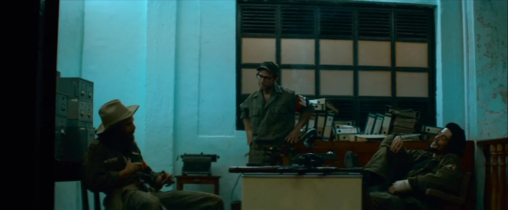 Che Part 1 (The Argentine) (2008) movie still: wide — A cluttered, utilitarian room features a large window with slats and stacked binders. Three…