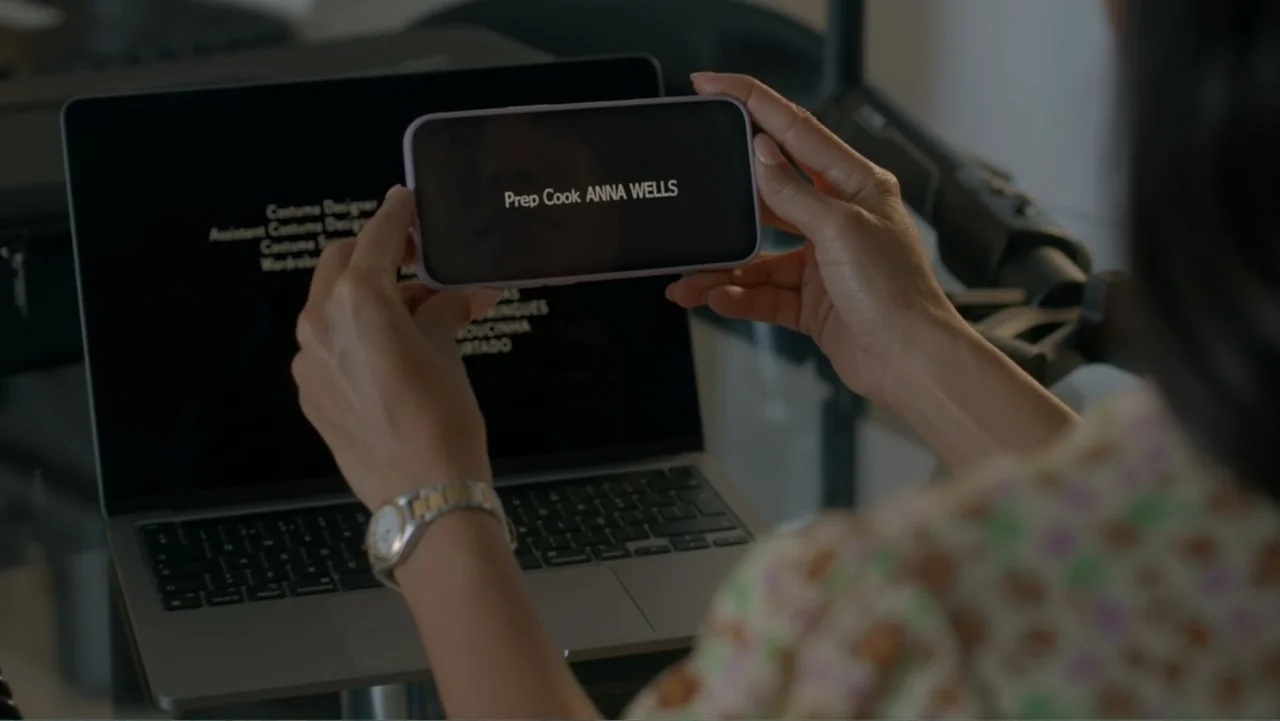 A Pinch of Portugal (2023) movie still: medium — An interior space features an open laptop and a smartphone held by a person. The phone screen…