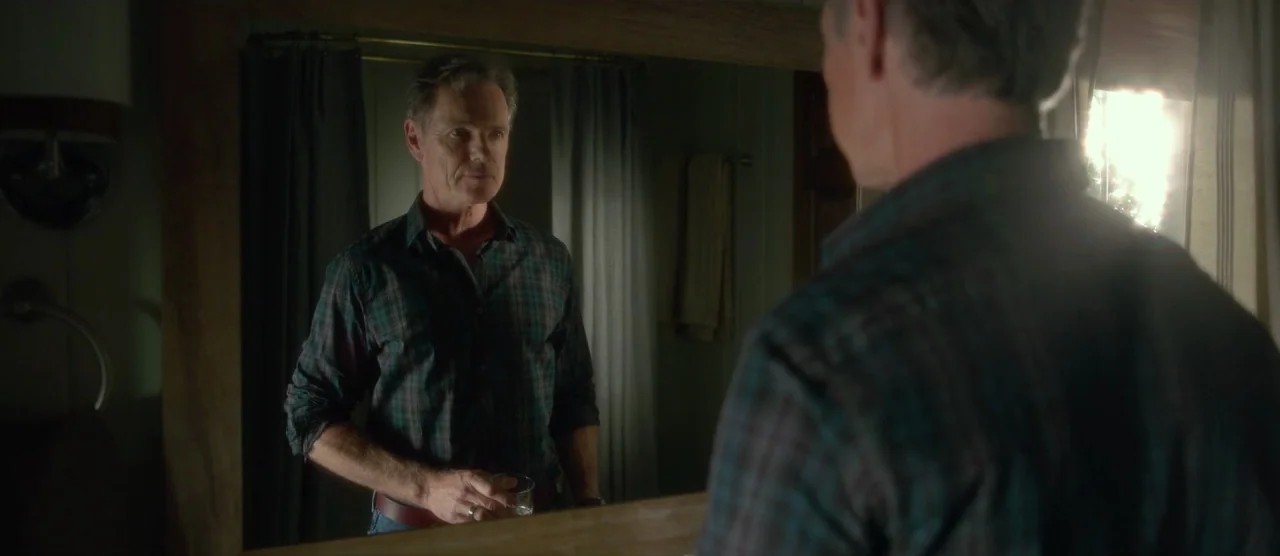 Gerald’s Game (2017) movie still: medium — A man in a plaid shirt stands before a large rectangular wall-mounted mirror. He stares at his own…