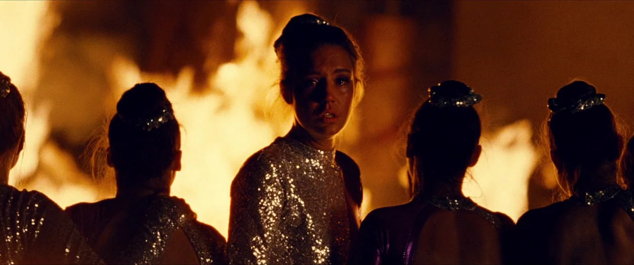 The Five Devils (2022) movie still: medium — Several women in sequined performance outfits stand in front of a roaring bonfire at night. One woman…