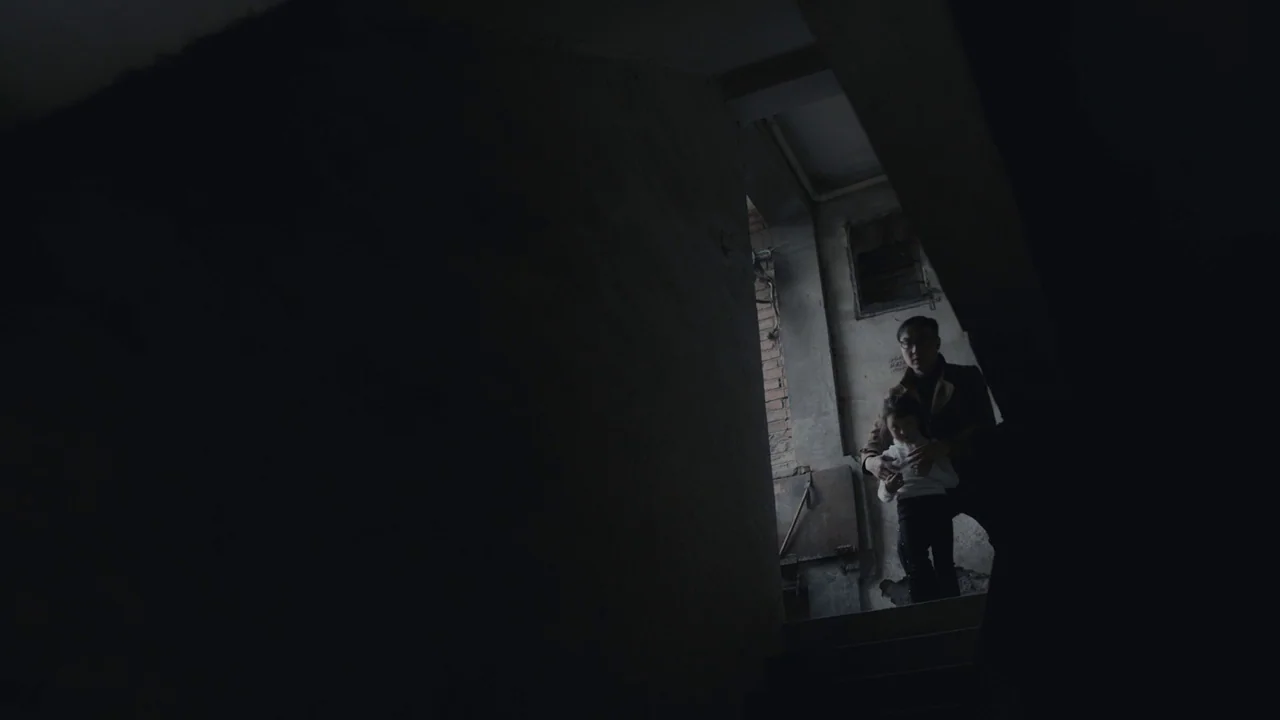 An Elephant Sitting Still (2018) movie still: wide — An industrial concrete stairwell with exposed brick walls and narrow steps. A man carries a…