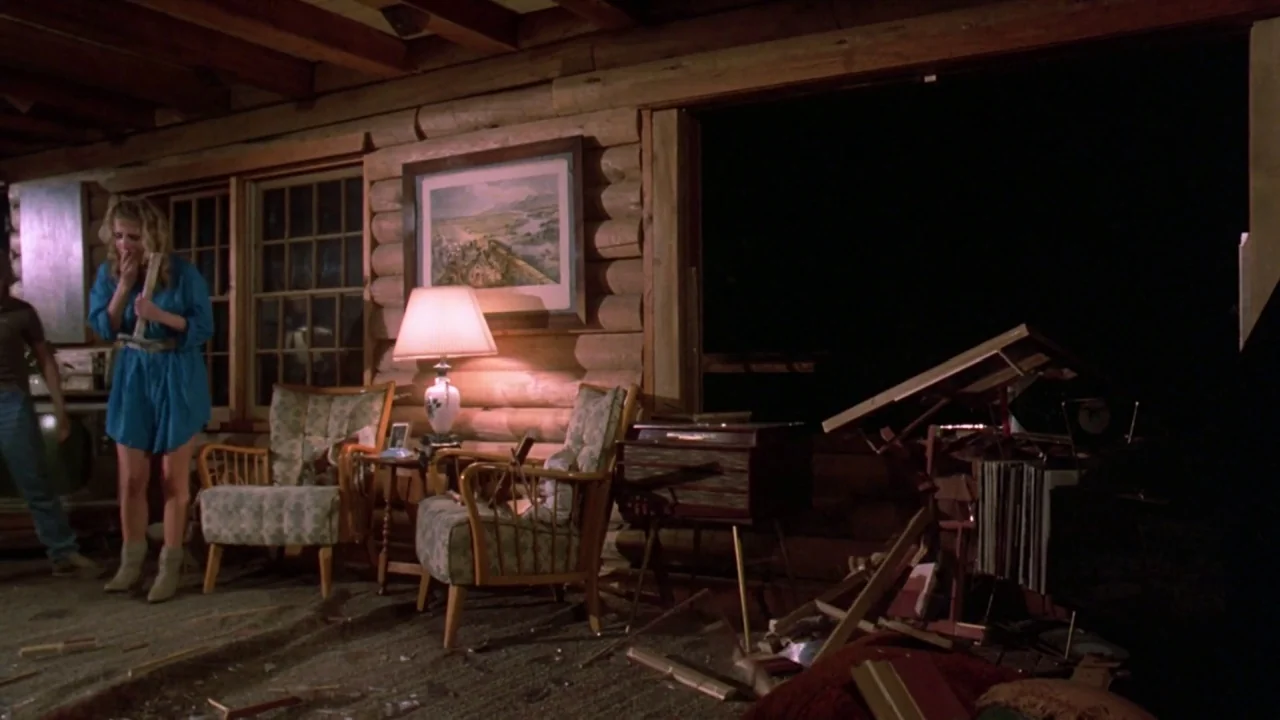 Friday the 13th: The Final Chapter (1984) movie still: wide — A rustic living room with log walls has a dark open window at night. A woman stands in…