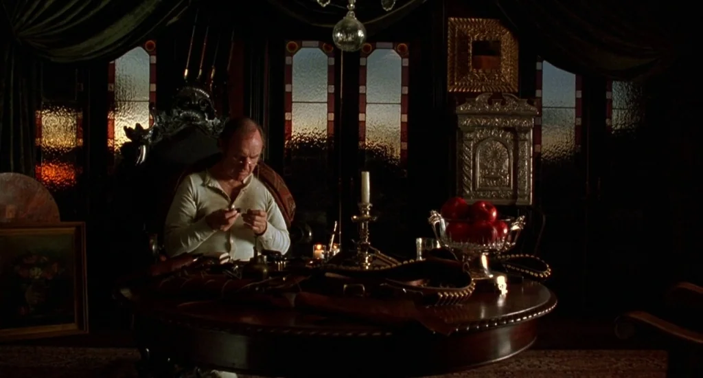 The Quick and the Dead (1995) movie still: medium — A dark wood-paneled room features a round table holding a crystal bowl of red apples. An elderly…