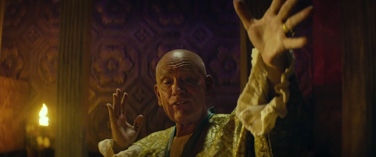 Seneca: On The Creation Of Earthquakes (2023) movie still: medium — A dimly lit room features textured purple wallpaper with floral patterns and…