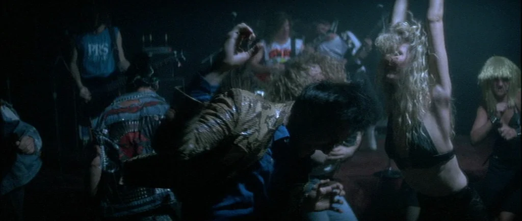 Wild At Heart (1990) movie still: medium — A dark, crowded music venue with several people dancing amidst blurred motion. A woman with long blonde…