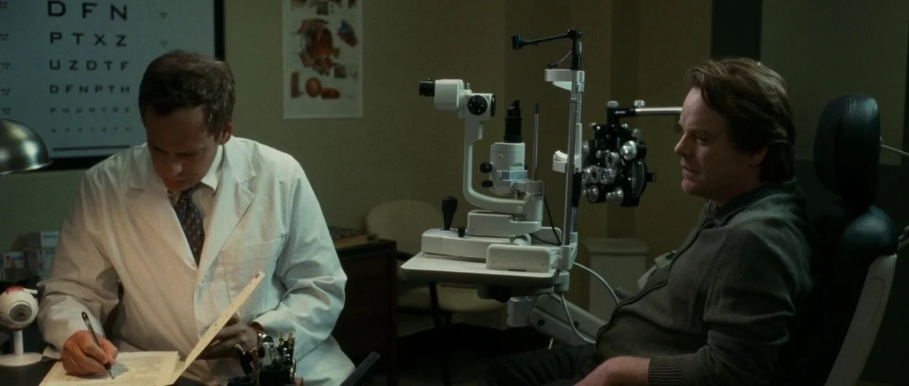 Synecdoche, New York (2008) movie still: medium — An optometrist office features a Snellen eye chart and a mechanical phoropter instrument. A doctor…